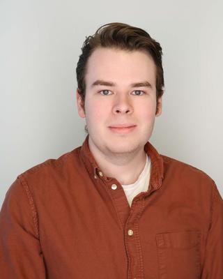 Male with brown short hair wearing a burnt orange button up shirt.