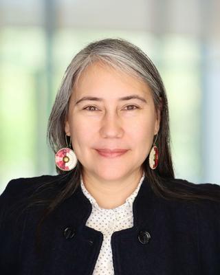Woman in black blazer and white collared shirt, headshot only.