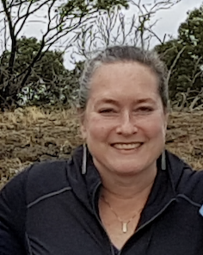 Headshot of female with hair pulled back, dangling earrings, black jacket, in a natural setting.